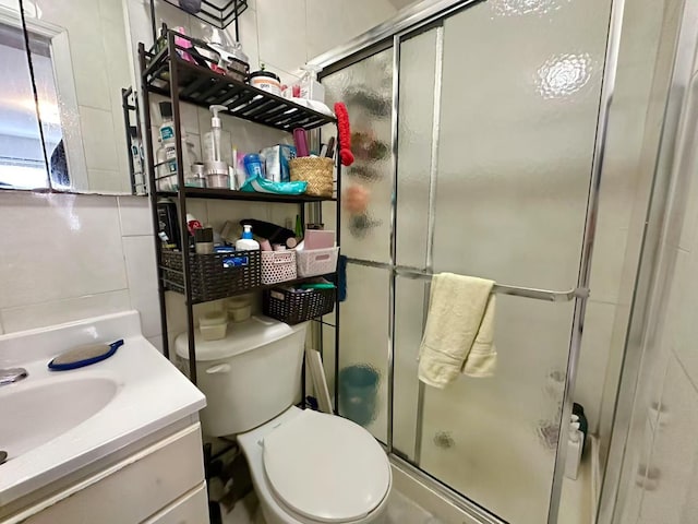 bathroom with toilet, tile walls, vanity, a shower with door, and decorative backsplash