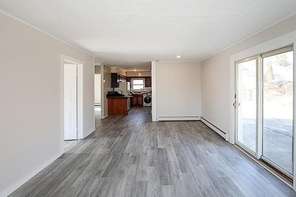 unfurnished living room with a baseboard radiator, washer / clothes dryer, ornamental molding, wood finished floors, and baseboards