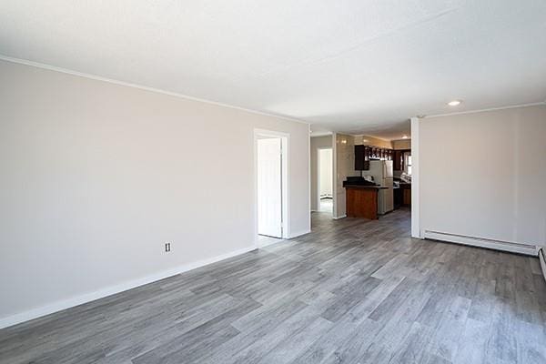 unfurnished living room with ornamental molding, a baseboard radiator, wood finished floors, and baseboards