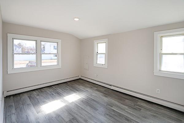 empty room featuring lofted ceiling, dark wood-style flooring, a healthy amount of sunlight, and baseboard heating