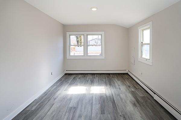 empty room with lofted ceiling, dark wood-style floors, baseboards, and a baseboard heating unit