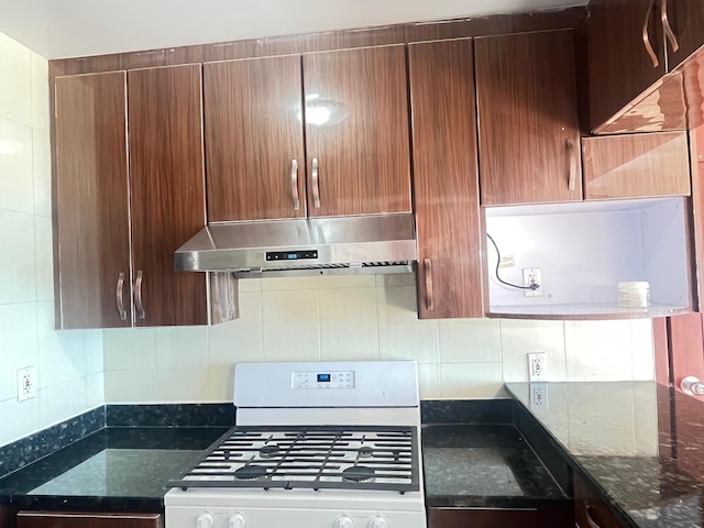 kitchen featuring white range with gas cooktop, decorative backsplash, exhaust hood, and dark stone countertops