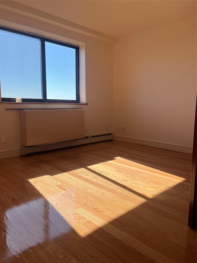 empty room featuring baseboard heating and hardwood / wood-style floors