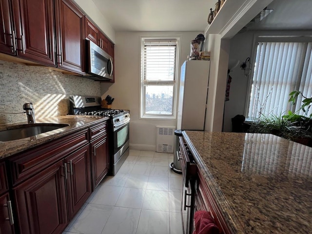 kitchen with reddish brown cabinets, decorative backsplash, stainless steel appliances, and a sink