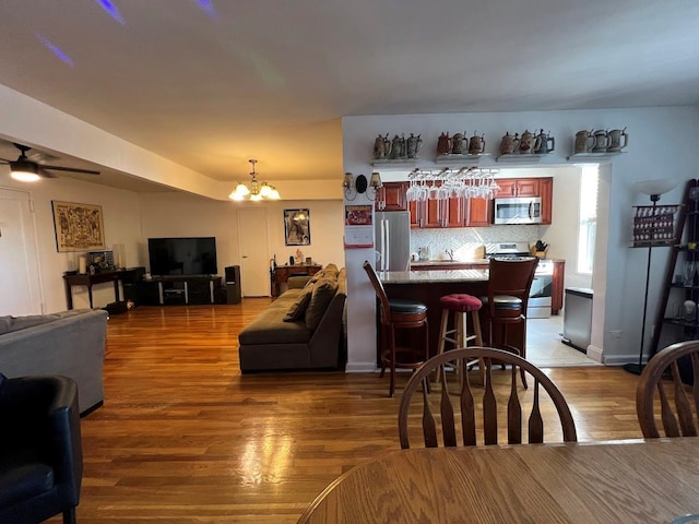 living room with a bar, wood finished floors, and ceiling fan with notable chandelier