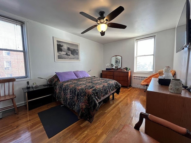 bedroom with a ceiling fan, radiator heating unit, baseboards, and light wood finished floors