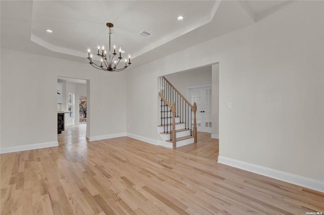 empty room featuring a notable chandelier, a tray ceiling, and light wood-type flooring