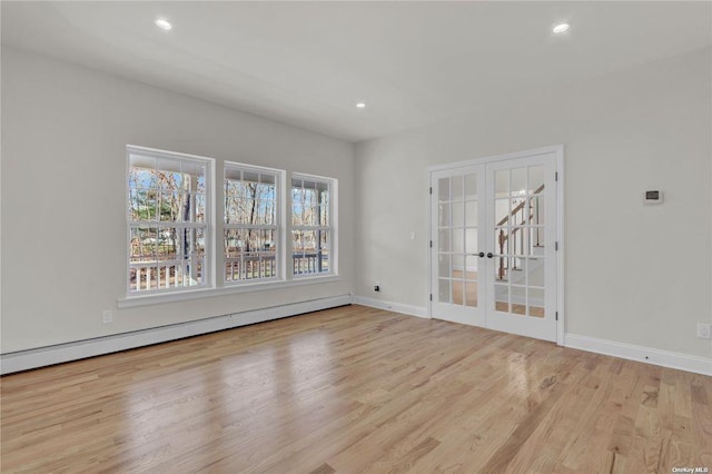 spare room featuring a healthy amount of sunlight, a baseboard heating unit, light hardwood / wood-style floors, and french doors