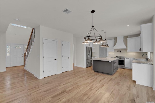 kitchen featuring pendant lighting, appliances with stainless steel finishes, white cabinetry, a kitchen island, and custom exhaust hood