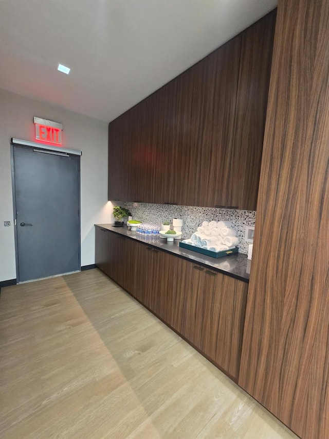 kitchen featuring light wood-style flooring, dark brown cabinets, tasteful backsplash, dark countertops, and modern cabinets