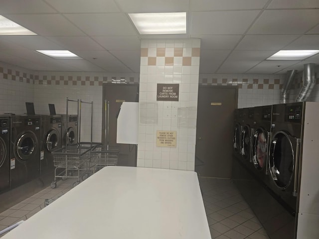 community laundry room featuring tile patterned flooring, washer and clothes dryer, and tile walls