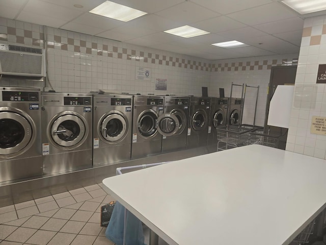 community laundry room featuring a wall unit AC, tile patterned flooring, separate washer and dryer, and tile walls