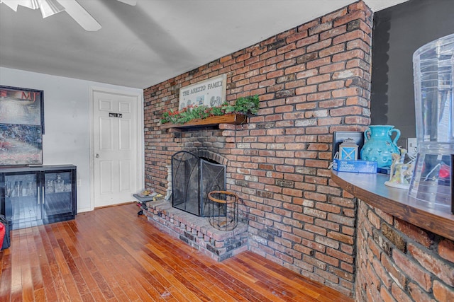 living room featuring a brick fireplace, brick wall, ceiling fan, and wood finished floors