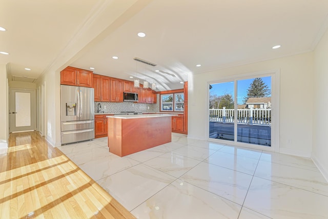 kitchen featuring appliances with stainless steel finishes, hanging light fixtures, a center island, ornamental molding, and decorative backsplash