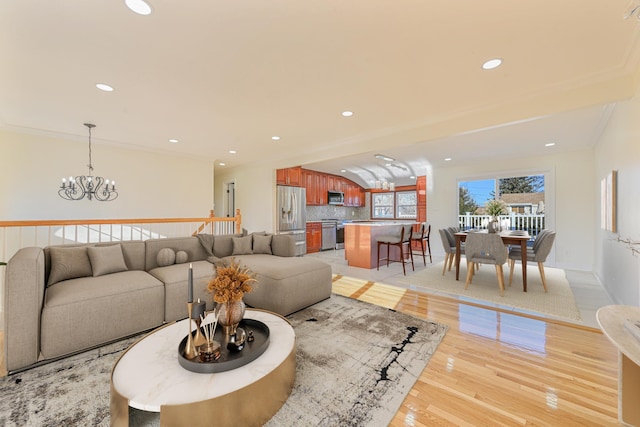 living room featuring an inviting chandelier, ornamental molding, and light hardwood / wood-style floors