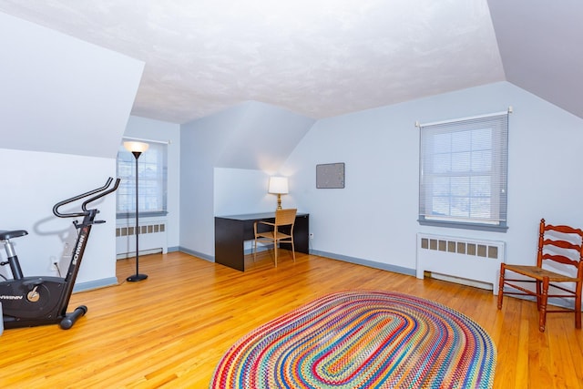 exercise area with hardwood / wood-style flooring, vaulted ceiling, and radiator