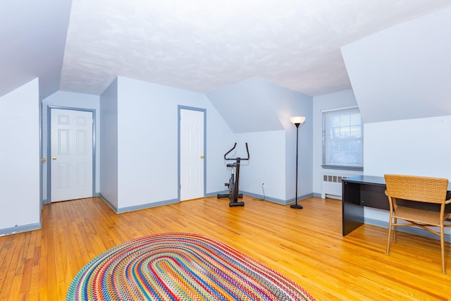 bonus room featuring vaulted ceiling, radiator heating unit, and light hardwood / wood-style floors