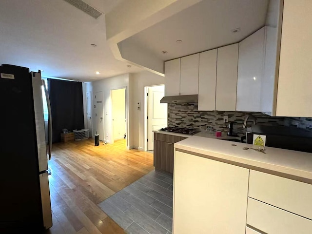 kitchen featuring stainless steel appliances, light wood-type flooring, decorative backsplash, and white cabinets