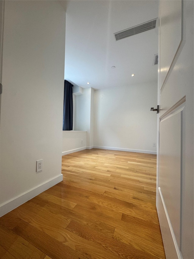 spare room with light wood-type flooring, visible vents, and baseboards