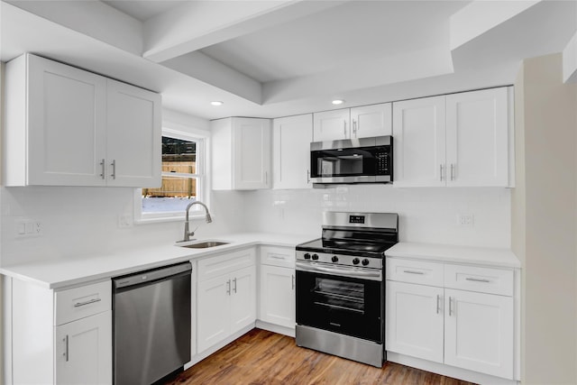 kitchen with stainless steel appliances, white cabinetry, sink, and light hardwood / wood-style floors