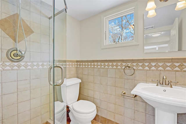 bathroom featuring toilet, sink, tile walls, and walk in shower