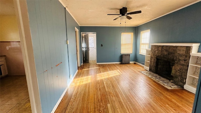 unfurnished living room featuring light hardwood / wood-style flooring, ceiling fan, radiator heating unit, a fireplace, and ornamental molding