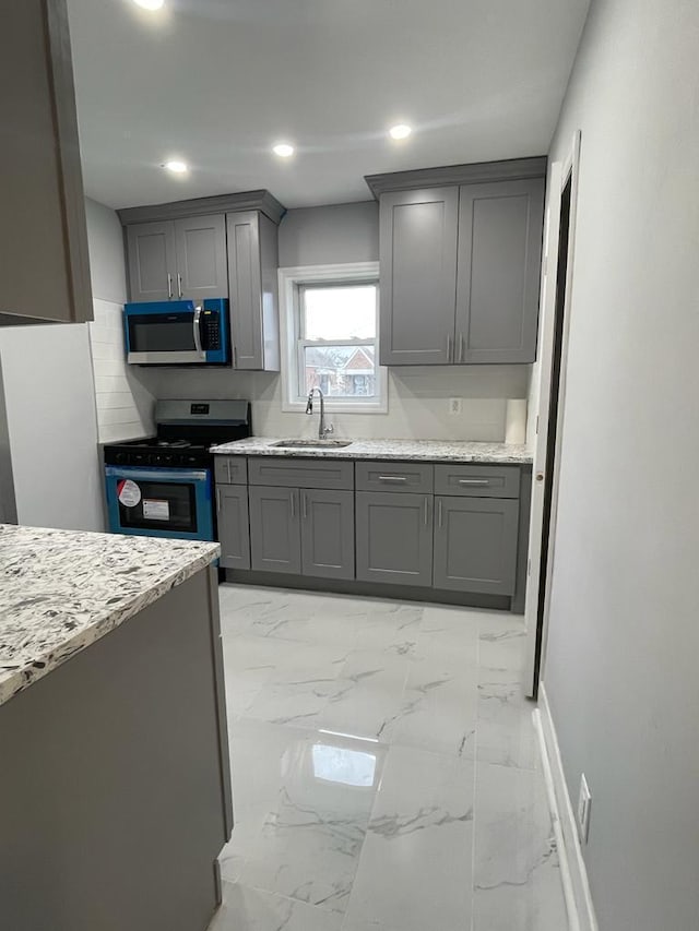 18806 Brinkerhoff Ave, Cambria Heights, NY 11412 - kitchen with stainless steel appliances, sink, light stone counters, and gray cabinets