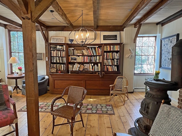 living area featuring a healthy amount of sunlight, a notable chandelier, beamed ceiling, and light wood-type flooring