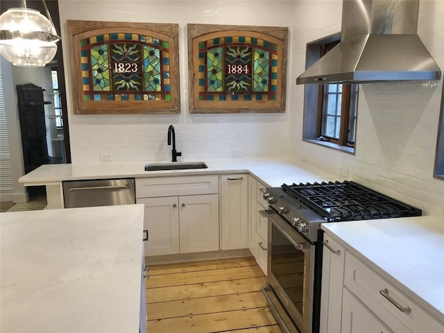 kitchen featuring pendant lighting, sink, white cabinets, stainless steel appliances, and wall chimney range hood