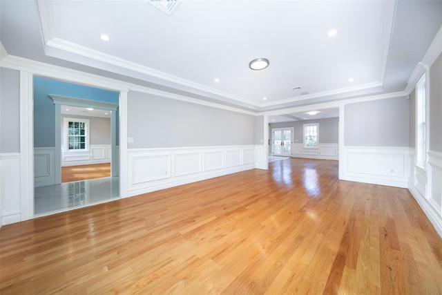 unfurnished living room featuring light wood-type flooring, visible vents, a raised ceiling, and ornamental molding