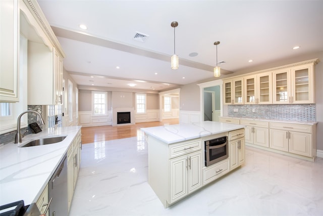 kitchen with decorative light fixtures, a sink, visible vents, open floor plan, and glass insert cabinets