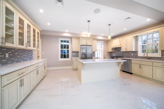 kitchen featuring visible vents, a kitchen island, glass insert cabinets, stainless steel appliances, and pendant lighting