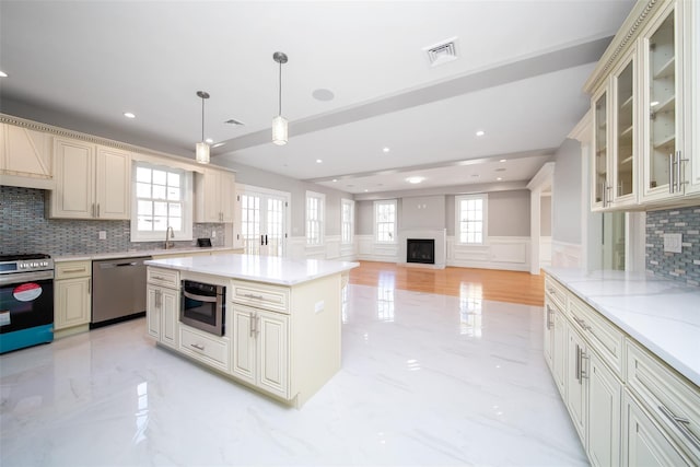 kitchen with marble finish floor, appliances with stainless steel finishes, cream cabinets, and pendant lighting