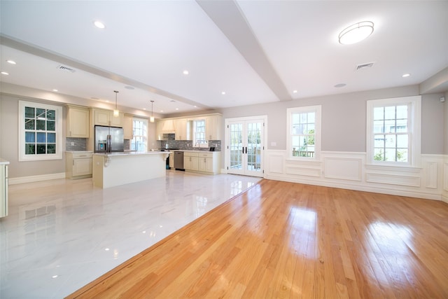 unfurnished living room with plenty of natural light, wainscoting, a decorative wall, and visible vents