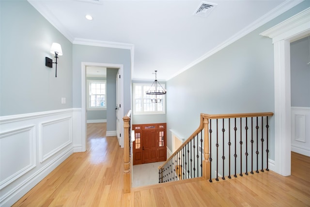 foyer entrance with crown molding, visible vents, light wood-style floors, wainscoting, and a chandelier