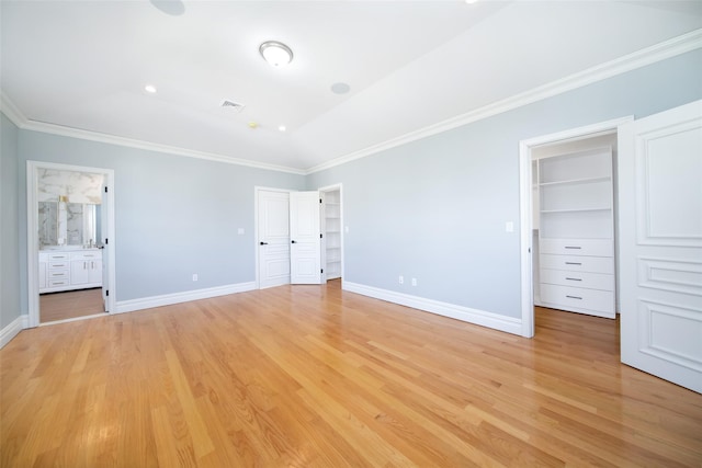 unfurnished bedroom featuring light wood finished floors, baseboards, visible vents, ornamental molding, and a walk in closet