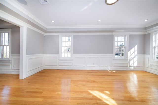 unfurnished room with light wood-type flooring, wainscoting, visible vents, and crown molding