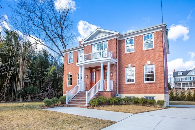 view of front of home featuring a balcony, a front lawn, and brick siding