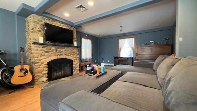 living room featuring hardwood / wood-style flooring, beam ceiling, and a stone fireplace