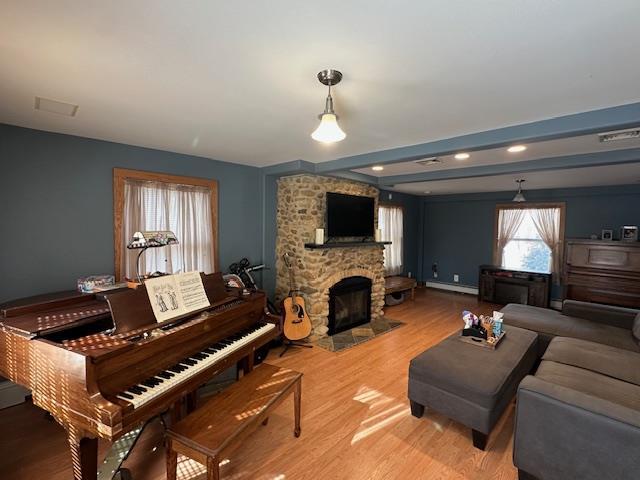 living room featuring a stone fireplace, light hardwood / wood-style floors, and baseboard heating