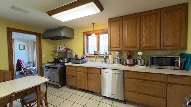 kitchen featuring light tile patterned flooring, decorative light fixtures, sink, stainless steel appliances, and wall chimney range hood