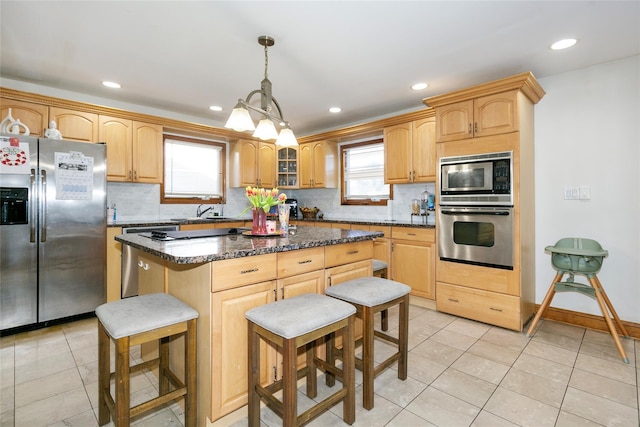 kitchen with hanging light fixtures, dark stone countertops, appliances with stainless steel finishes, a kitchen island, and decorative backsplash