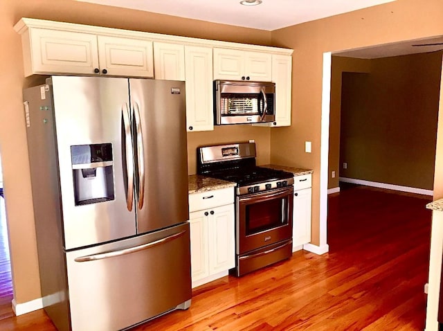 kitchen featuring stainless steel appliances, white cabinetry, light hardwood / wood-style flooring, and dark stone counters