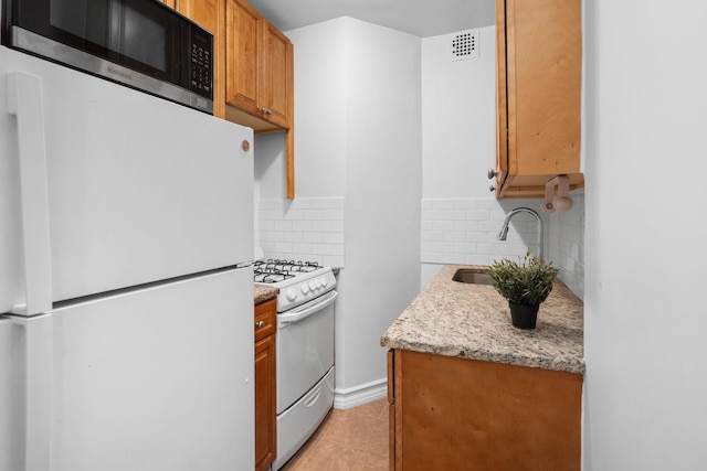 kitchen with sink, white appliances, light tile patterned floors, backsplash, and light stone counters