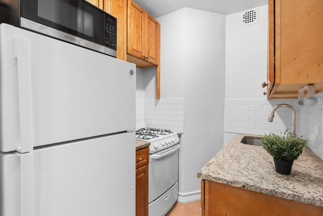 kitchen featuring sink, tasteful backsplash, light tile patterned floors, white appliances, and light stone countertops