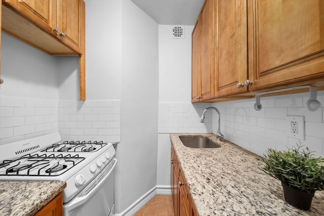 kitchen featuring sink, light tile patterned floors, light stone counters, and gas range gas stove