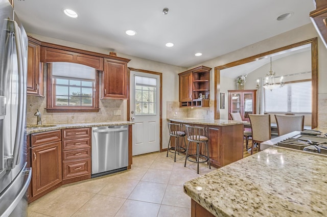 kitchen with light stone counters, hanging light fixtures, stainless steel appliances, and a breakfast bar