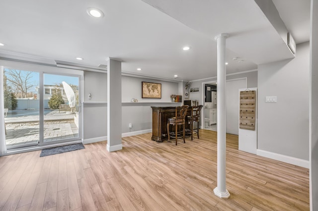 interior space with ornate columns, crown molding, bar, and light hardwood / wood-style floors