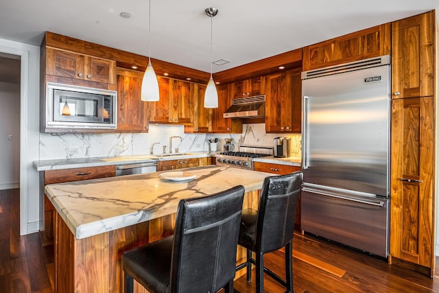 kitchen with tasteful backsplash, built in appliances, hanging light fixtures, and a kitchen island