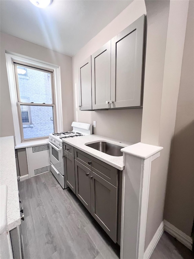 kitchen with sink, gray cabinetry, light wood-type flooring, radiator heating unit, and white gas range